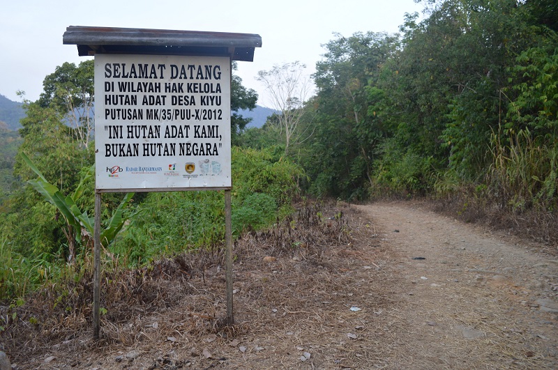 A sign next to a dirt road reads in Indonesian, ‘Welcome to the territory of the Kiyu customary forest under Constitutional Court Decree No. 35/PUU-X/2012. THIS IS OUR CUSTOMARY FOREST, NOT STATE FOREST.’