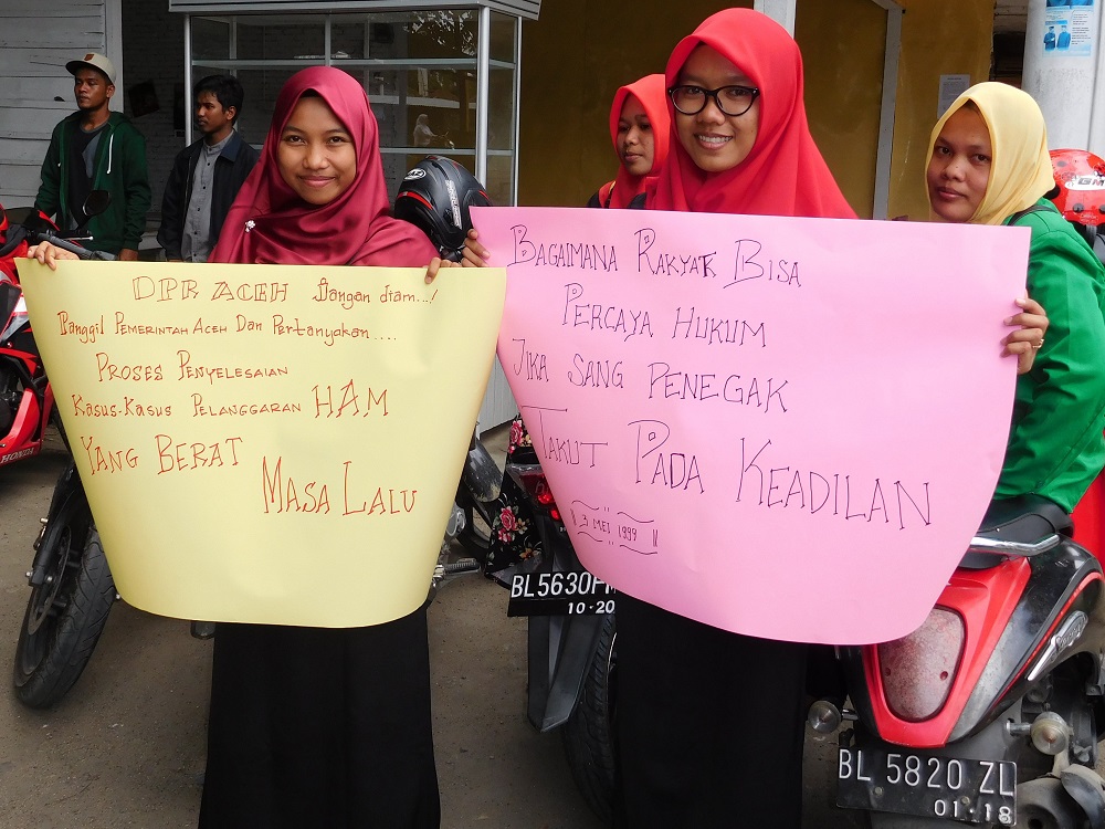 Two Acehnese young women hold up colourful protest signs demanding justice for past human rights violations.