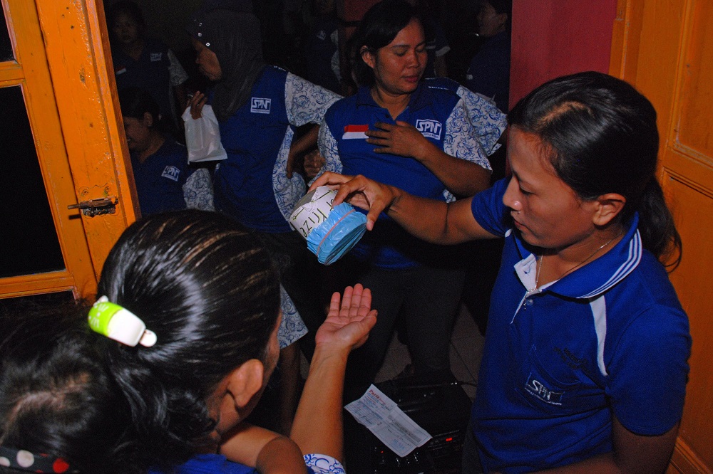 A woman tips a coin tin over another woman's open palm.