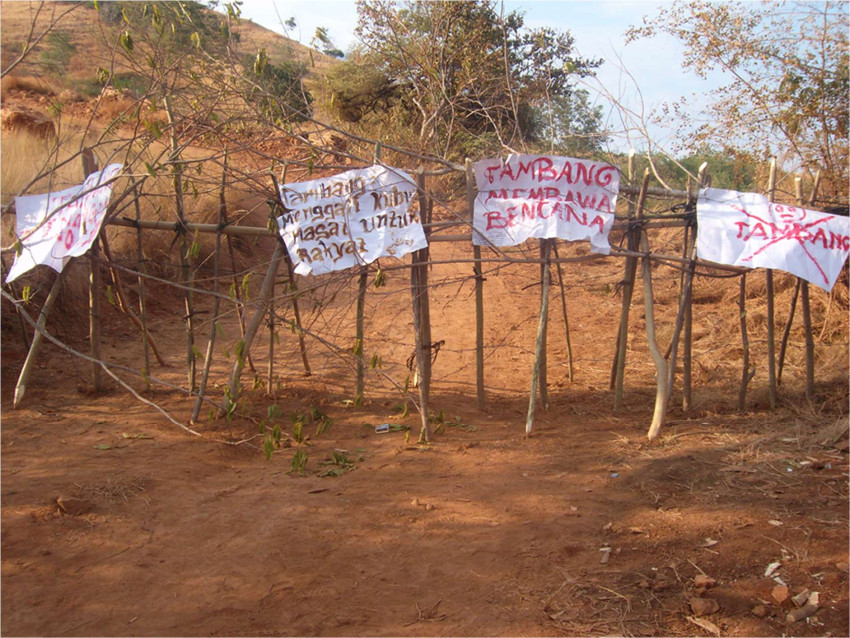 Paper signs protesting mining flutter in the wind, attached to a fence.