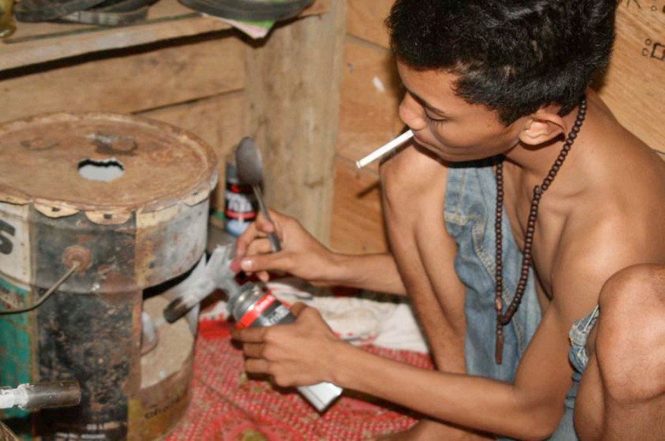 A child worker in a squatting position, burning mercury amalgam while smoking a cigarette.